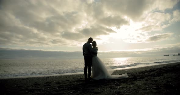 Kissing Wedding Couple Stands Against the Sunset on a Beach in Iceland.