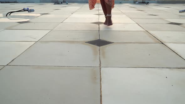 Ascending view of young blond attractive woman walking barefoot on terrace in flowing orange skirt w