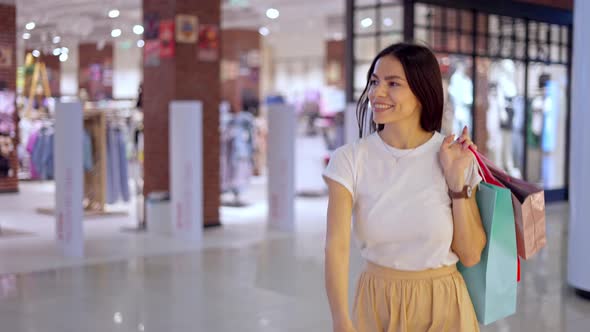 Happy Woman Leaving Store in Shopping Mall with Many Paper Bags Full of Purchases
