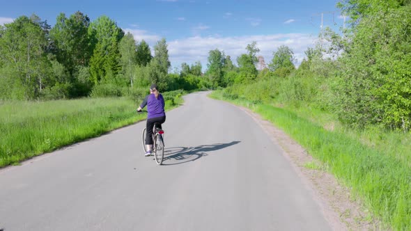 View of woman on bicycle moving on small road on beautiful countryside landscape background.