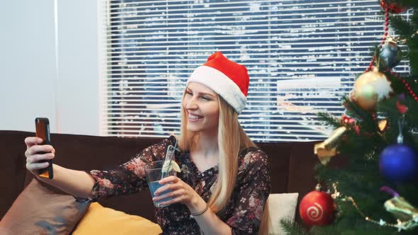 Side View of Good-looking Woman Making Selfie in Santa Hat and with Drink in Her Hands