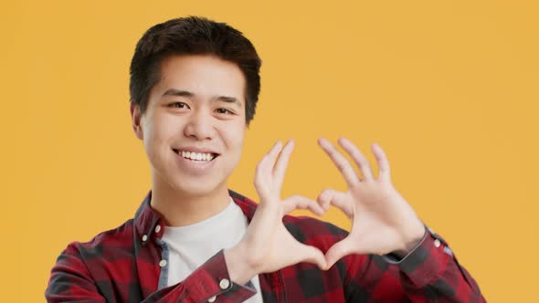 Cheerful Asian Guy Showing HeartShape Gesture Posing Over Yellow Background