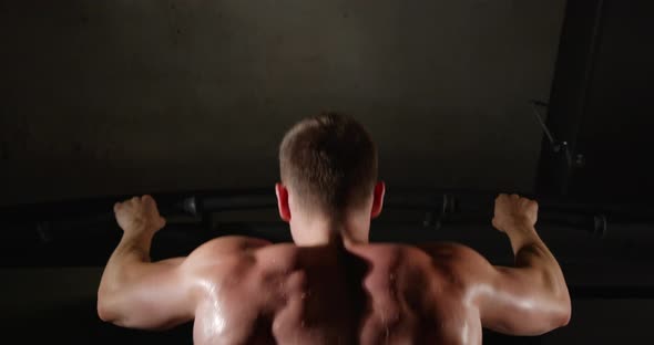 A man with beautiful muscles on his back, in the gym, pulls himself up on a horizontal bar