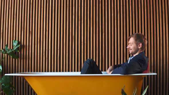 Happy Rich Businessman Lying in a Bathtub Filled with Money