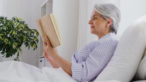 Senior Woman Reading Book in Bed at Home Bedroom