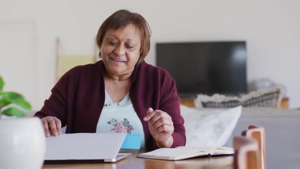 Happy african american senior woman at dining table, closing laptop and smiling