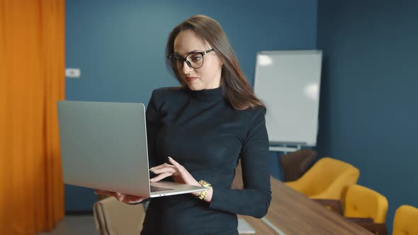 Confident and Smiling Business Woman in Glasses of Caucasian Appearance Working on Laptop Holding