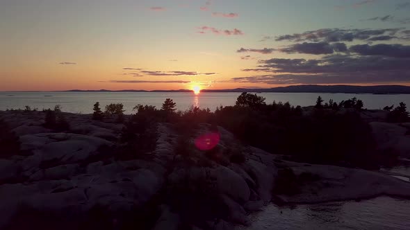 Flying over Rocky Pine Tree Island in Blue Lake at Sunset, Drone Aerial Wide Dolly In. Colorful Clou