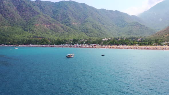 Aerial view of a single tourist boat in the blue tropical sea of Adrasan beach in Turkey and a busy