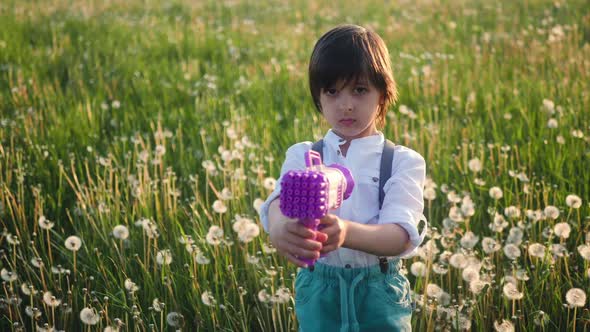 Portrait of a Five Year Old Boy in a Hat Stands on a Field of Dandelions and Shoots Soap Bubbles