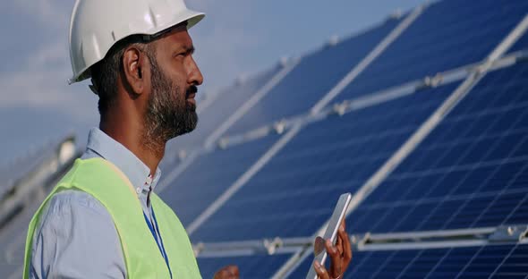 Close Up of Mixed Race Male Worker Looking at Tablet Screen and Solar Panel. Man in Hard Helmet and