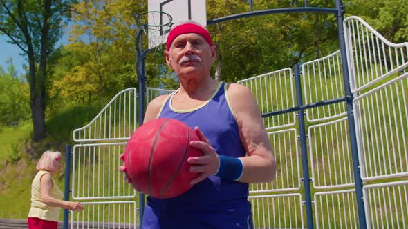 Senior Man Grandfather Athlete Posing with Ball Looking at Camera on Playground Basketball Court