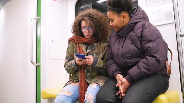 Two young multiethnic women travelling underground using smart phone