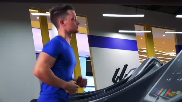 A Young Fit Man Jogs on a Treadmill in a Gym - View From Side