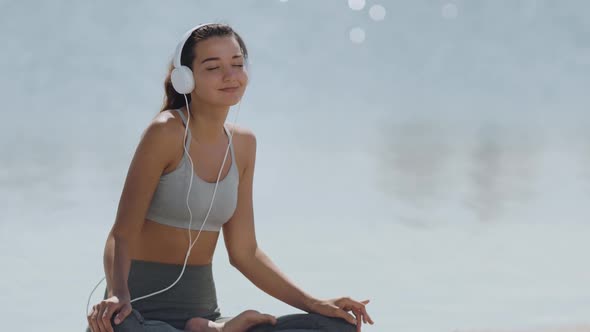 Woman in Yoga Meditation Pose with Headphones on the Beach