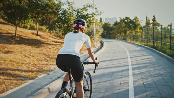 Woman in Protective Helmet is Riding Her Bicycle Along the Bike Path in a Park Planted with Green