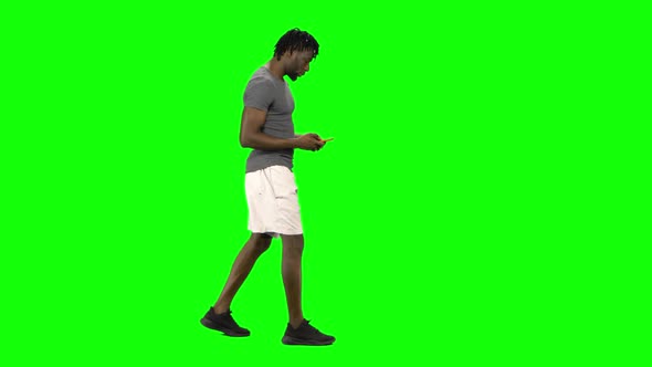 African American Man Walking and Texting Message Vie His Mobile Phone at Green Screen, Chroma Key