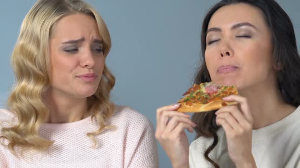 Asian Woman Greedily Eating Pizza in Front of Her Friend Who Keeping Diet