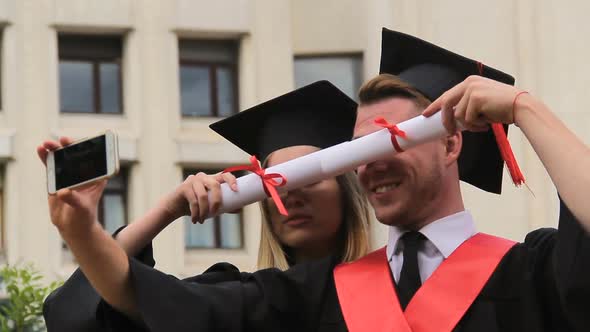 Female and Male Graduates in Academic Dresses and Caps Shooting Video on Phone