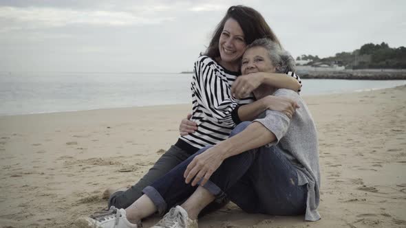 Happy Adult Daughter and Senior Mother Sitting on Sand