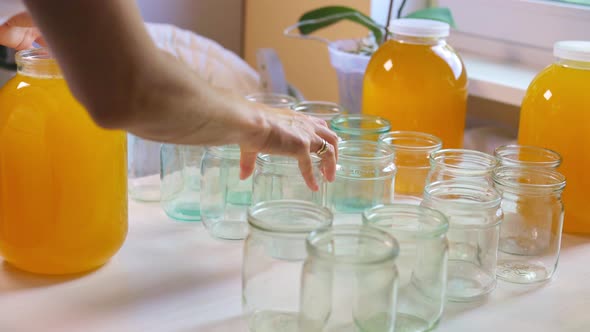 Woman Pours Honey Into Transparent Jars on a White Table