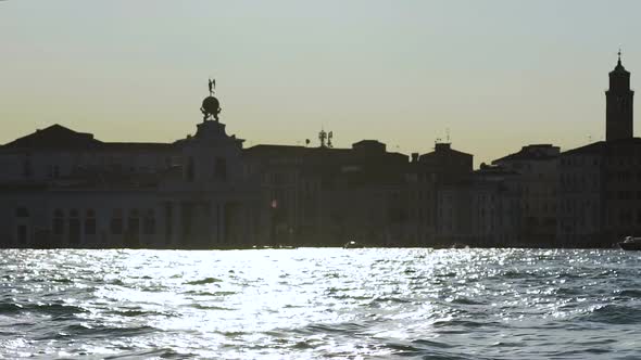 Ruffled River with Sunlight Reflected Off Water, Silhouette of Buildings at Back