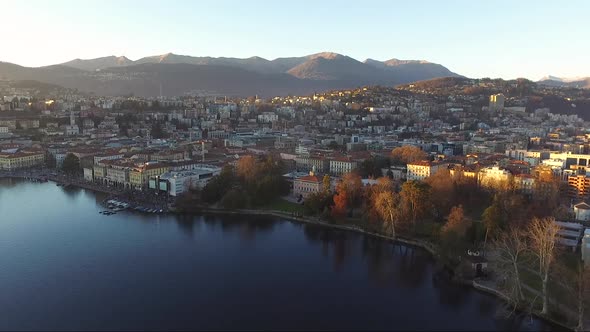 A drone view of a beautiful town surrounded by mountains, next to a lake, during a sunset in autumn.