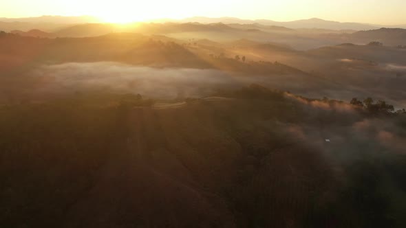 Aerial view of sunrise with fog above mountains. Golden hour and amazing sun rays. Nan, Thailand