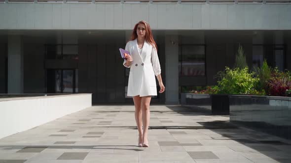 Beautiful business woman with notebook in her hands walk to office in heels work