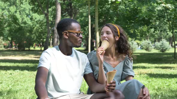 Black Man and Brunette Eat Organic Icecream on Grass Lawn