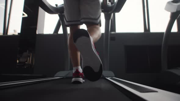 Closeup of Legs Man Jogging on Treadmill in Gym Back View