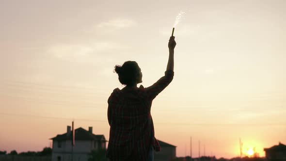 Young Woman Standing with Firework Candles During Sunset and Looking in the Camera