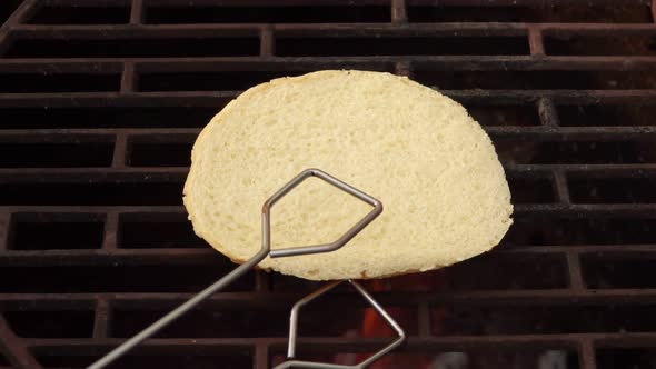 Closeup of Burger Bun Flipped on the Grill Grid with Kitchen Tongs