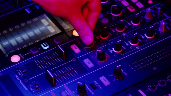 DJ Moves Fader to Increase Volume of Music on Mixing Console Illuminated By Neon Lights in Nightclub