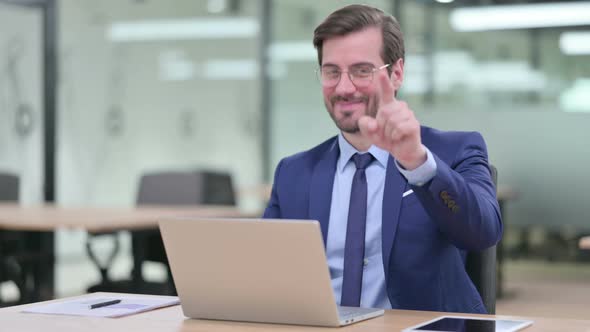 Serious Young Businessman with Laptop Pointing at the Camera 