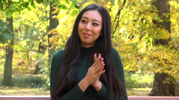 A Young Asian Woman Sits on A Bench in A Park and Celebrates