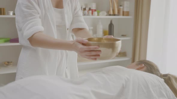 Massage Takes Singing Bowl for Sound Therapy and Puts on Back Lying Woman