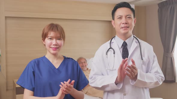 Portrait of Asian doctor and nurse giving encouragement to patient by clapping the hands in hospital