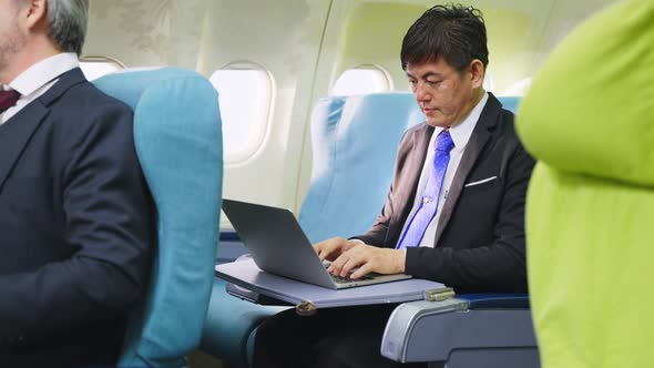 Asian businessman sitting in business class working on laptop computer on airplane for business .