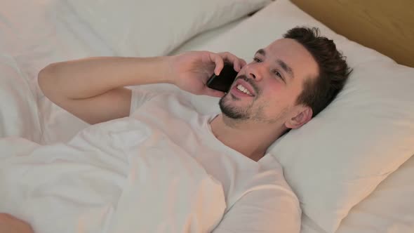 Young Man Talking on Smartphone in Bed