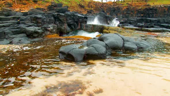 Water splashes up through a narrow channel along a rocky coastline beside the ocean