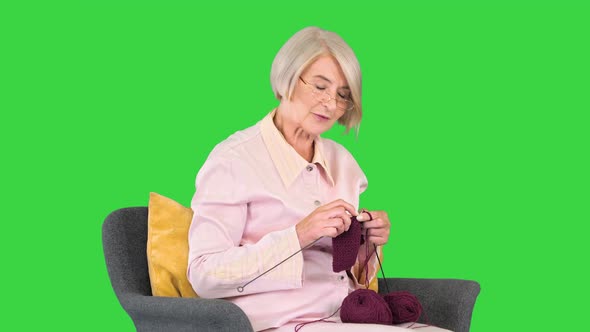 Mature Grandmother Sitting and Knitting and Telling a Story To Camera on a Green Screen Chroma Key