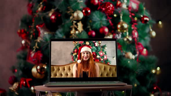 Woman with in Santa Hat Sits in Splits Holds Out New Year's Gift Via a Laptop