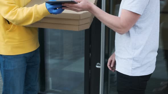 Delivery Man Wearing Protective Mask and Rubber Gloves Delivers Pizza Order to a Young Male Customer