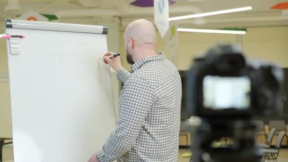 Teacher Records Video Lessons He Stands and Writes with a Pen on a Flip Chart