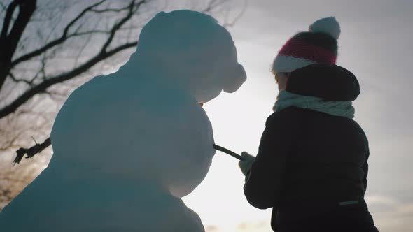 Happy Girl Builds a Snowman in Winter Park