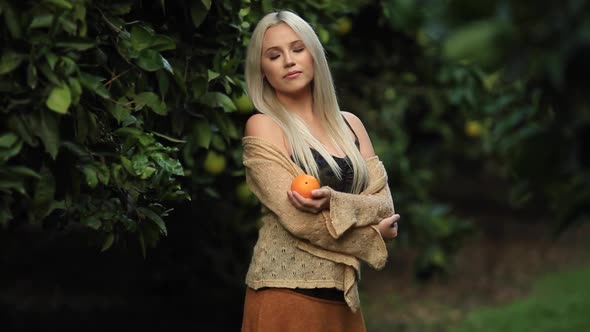 Woman Blonde with Closed Eyes Holding an Orange in Her Hands