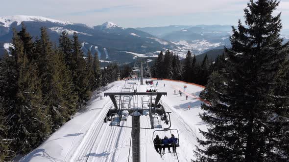 Drone Flies Over Ski Lift and Snowy Ski Slope with Skiers on Top of Mountain