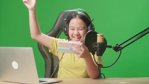 Asian Kid Girl Holding Mobile Phone And Talking To Camera While Live Stream On Green Screen