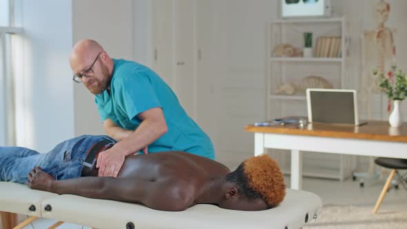 A Physical Therapist Is Giving Massage Therapy To a Black Man Who Is Lying on a Couch